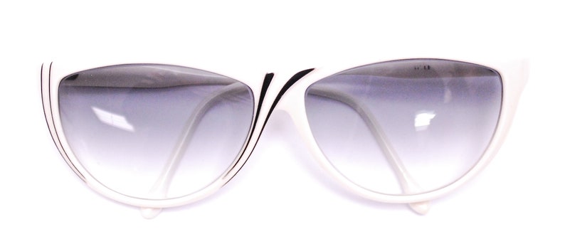 May include: White cat-eye sunglasses with black trim and gradient grey lenses.