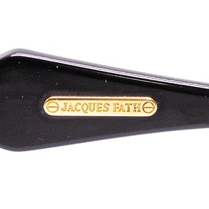 Op de afbeelding: Close-up van een zwart plastic frame met een gouden metalen plaat waarop "JACQUES FATHE" staat.
