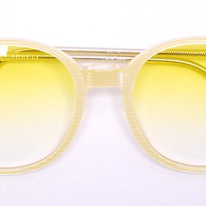 May include: A pair of yellow tinted round sunglasses with a cream colored frame. The frame has a textured pattern.