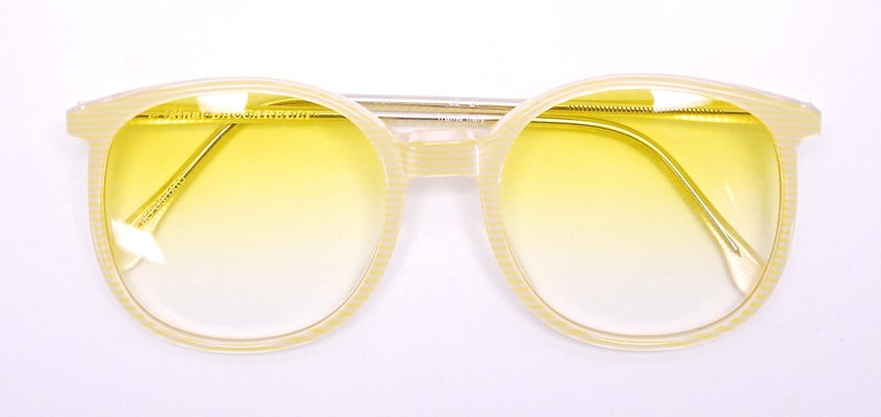 May include: A pair of yellow tinted round sunglasses with a cream colored frame. The frame has a textured pattern.