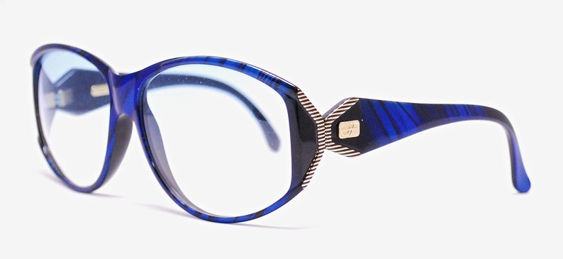 Op de afbeelding: Blauwe en zwarte gepatroneerde bril met een gouden accent aan de zijkant. De glazen hebben een blauwe tint.