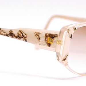 May include: Beige and brown patterned plastic sunglasses with a light brown gradient lens.