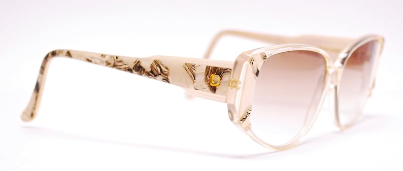 May include: Beige and brown patterned plastic sunglasses with a light brown gradient lens.