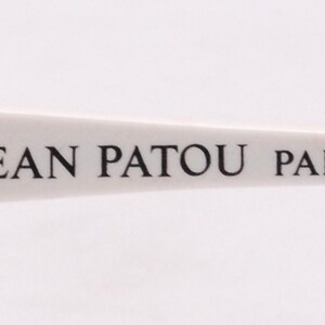 Peut inclure: Gros plan sur une monture en plastique blanche avec le texte "JEAN PATOU PARIS" imprim&eacute; en noir.
