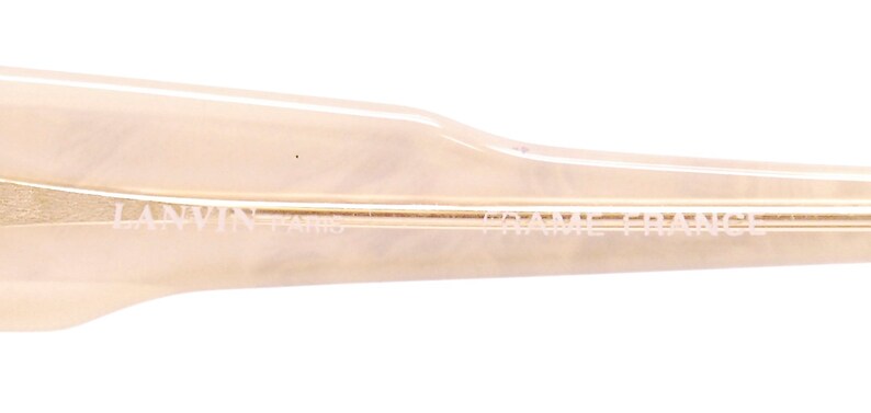May include: Close-up of the side of a pair of beige sunglasses with the text "LANVIN - PARIS - FRAME FRANCE" printed on the frame.