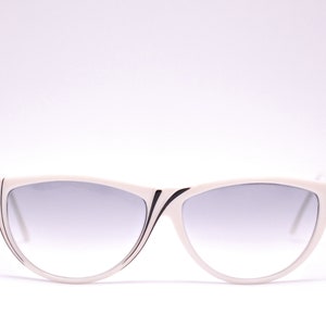 May include: White cat-eye sunglasses with black trim and gradient grey lenses.