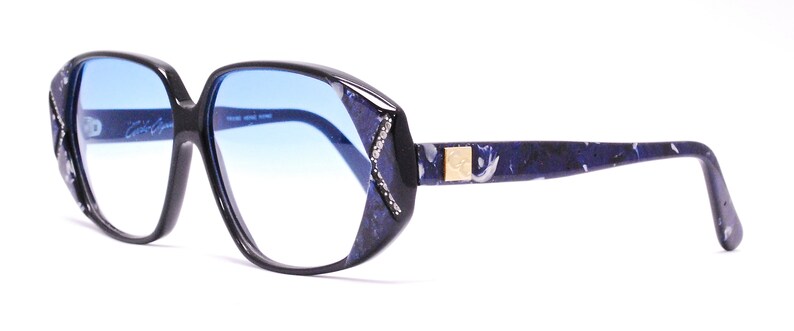 May include: Black and blue patterned eyeglasses with blue tinted lenses. The brand name "Calvin Klein" is printed on the left lens.