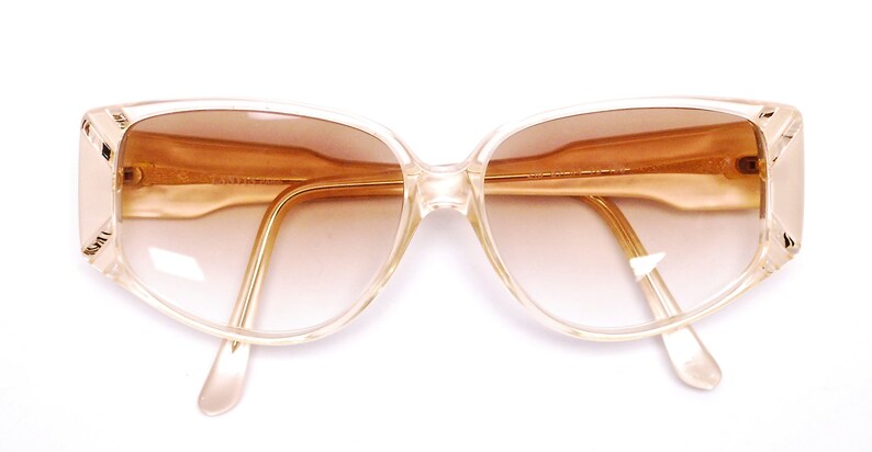 May include: A pair of clear, plastic framed sunglasses with brown gradient lenses. The sunglasses have a cat-eye shape.
