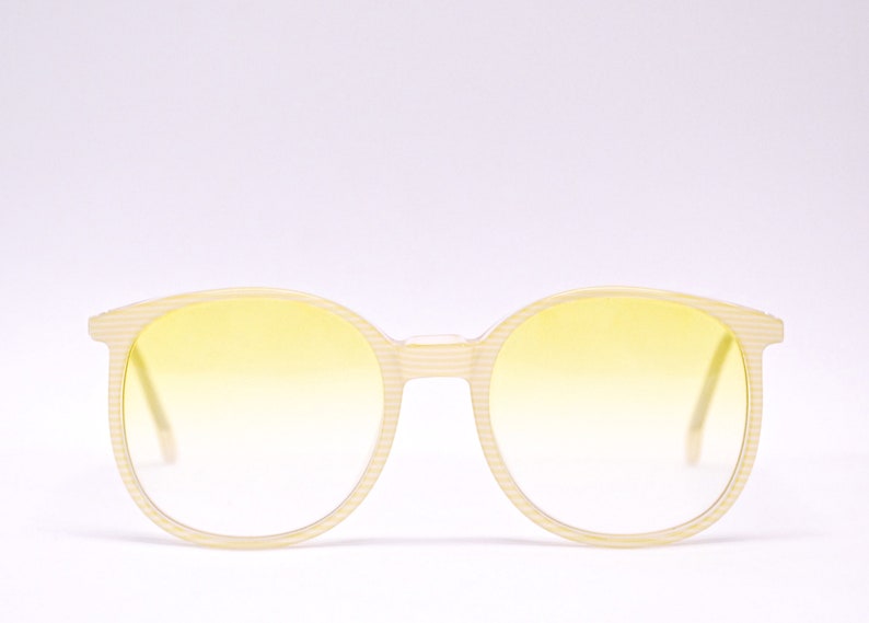 May include: A pair of round, yellow-tinted sunglasses with a white striped frame.