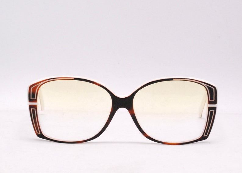 Peut inclure: Une paire de lunettes de vue en &eacute;caille de tortue avec des montures blanches et une bordure blanche autour des verres.