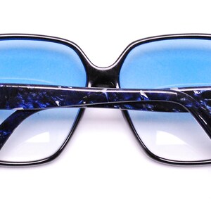 May include: Black sunglasses with blue tinted lenses and a blue and white marbled pattern on the arms. The sunglasses have gold CC logos on the arms.