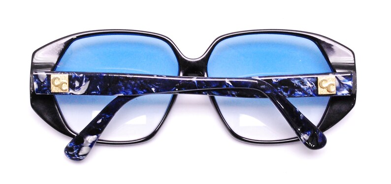 May include: Black sunglasses with blue tinted lenses and a blue and white marbled pattern on the arms. The sunglasses have gold CC logos on the arms.