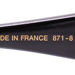 Op de afbeelding: Close-up van de zwarte poot van een bril met gouden letters die "MADE IN FRANCE 871 -8 JF 42" lezen.