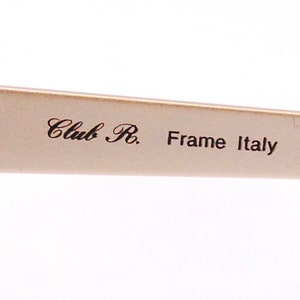 Op de afbeelding: Close-up van een beige brilmontuur met de tekst "Club R. Frame Italy" erop gedrukt.