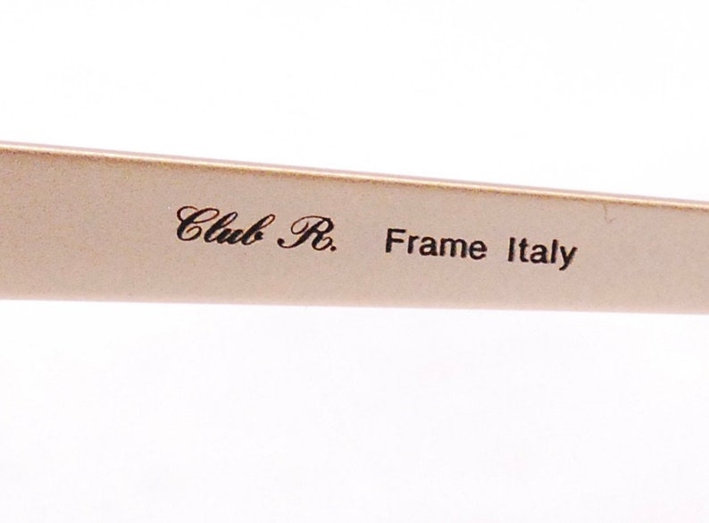 Op de afbeelding: Close-up van een beige brilmontuur met de tekst "Club R. Frame Italy" erop gedrukt.