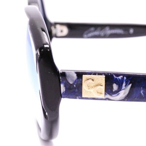 May include: Black sunglasses with blue and white marbled frames and gold CC logo. The sunglasses have a blue mirrored lens.