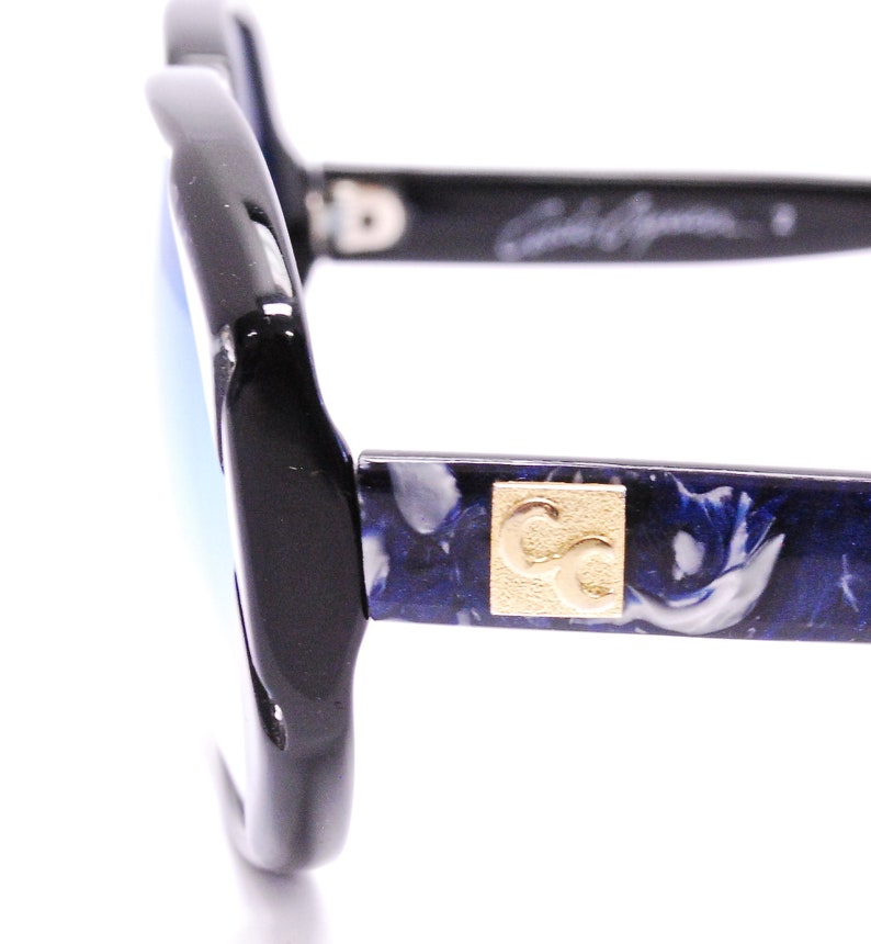 May include: Black sunglasses with blue and white marbled frames and gold CC logo. The sunglasses have a blue mirrored lens.