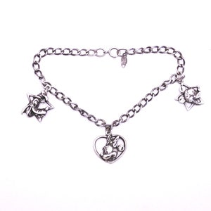 May include: A silver charm bracelet with three charms: a heart, a star, and a flower. The heart charm features a cartoon character.
