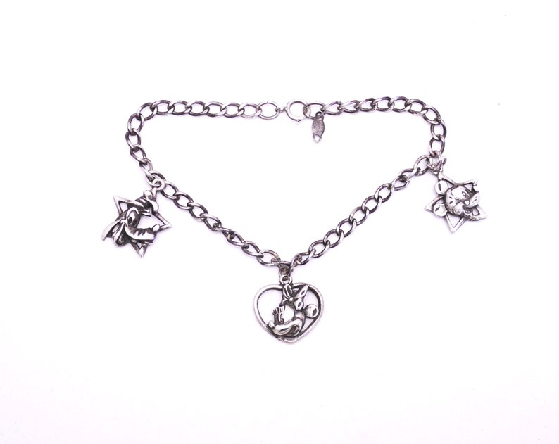 May include: A silver charm bracelet with three charms: a heart, a star, and a flower. The heart charm features a cartoon character.