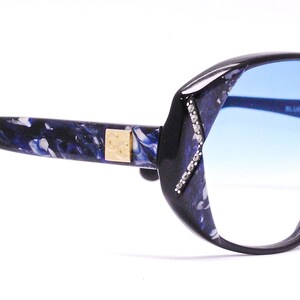 May include: Black and blue patterned eyeglasses with blue gradient lenses. The lenses are oval shaped and the frame is thick and wide.
