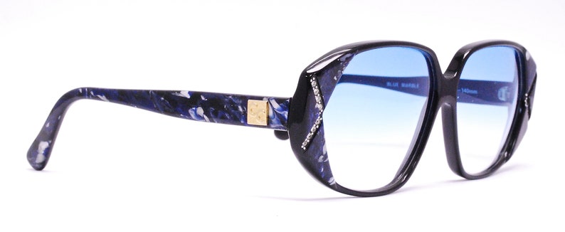 May include: Black and blue patterned eyeglasses with blue gradient lenses. The lenses are oval shaped and the frame is thick and wide.