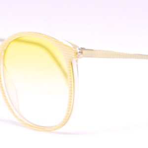 May include: A pair of yellow tinted sunglasses with a light brown frame. The frame has a textured pattern.