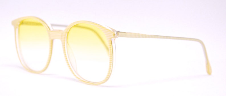 May include: A pair of yellow tinted sunglasses with a light brown frame. The frame has a textured pattern.