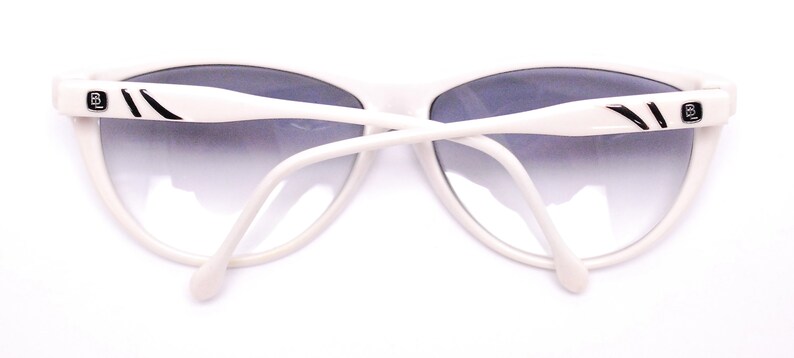 May include: White cat-eye sunglasses with black accents and a gradient lens.