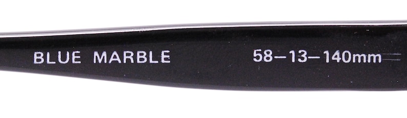 May include: Close-up of the inside of a black eyeglass frame with the text "BLUE MARBLE 58-13-140mm" printed in white.