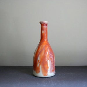 May include: A ceramic vase with a white and orange marbled glaze. The vase has a narrow neck and a wide base.