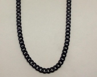 Puede incluir: Un collar de cadena negro con un diseño de eslabones de acera. El collar está hecho de un material oscuro y brillante y se muestra sobre un fondo blanco. La cadena es de estilo clásico.