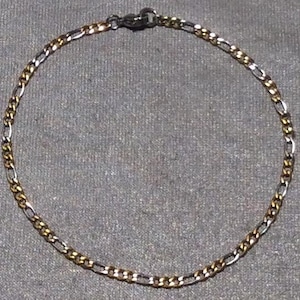 May include: A silver and gold chain bracelet with a lobster clasp.