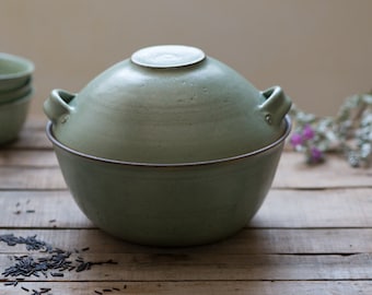 Puede incluir: Un bol de cerámica verde con tapa, perfecto para servir arroz u otros platos. El bol tiene un diseño simple y elegante y está hecho de materiales de alta calidad.