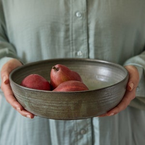 May include: A person holding a dark green ceramic bowl filled with red pears.