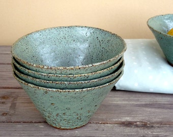 May include: Stack of four light blue ceramic bowls with a speckled glaze. The bowls are nested together and have a rounded shape.