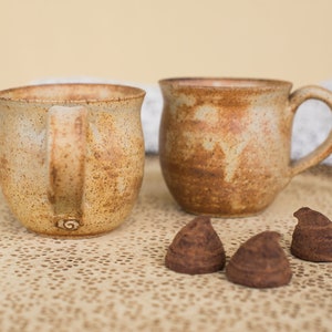 May include: Two brown ceramic mugs with speckled glaze on a tray with three dark chocolate truffles.