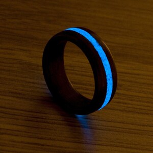 Puede incluir: Un anillo de madera negro con una franja azul que brilla en la oscuridad.