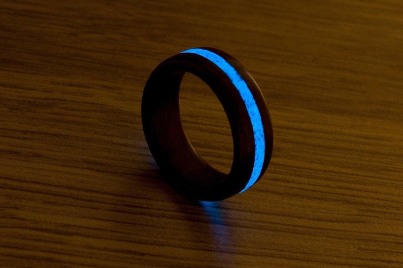 Puede incluir: Un anillo de madera negro con una franja azul que brilla en la oscuridad.