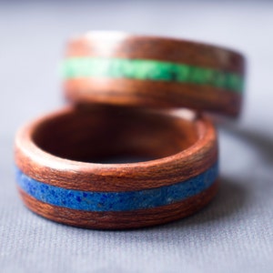 Puede incluir: Dos anillos de madera con bandas de piedra azul y verde incrustadas. Los anillos est&aacute;n apilados uno encima del otro.