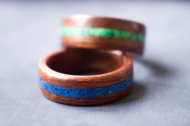 Puede incluir: Dos anillos de madera con bandas de piedra azul y verde incrustadas. Los anillos est&aacute;n apilados uno encima del otro.