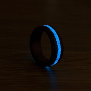 Puede incluir: Un anillo de madera negro con una incrustaci&oacute;n azul que brilla en la oscuridad. El anillo est&aacute; sobre una superficie de madera oscura.