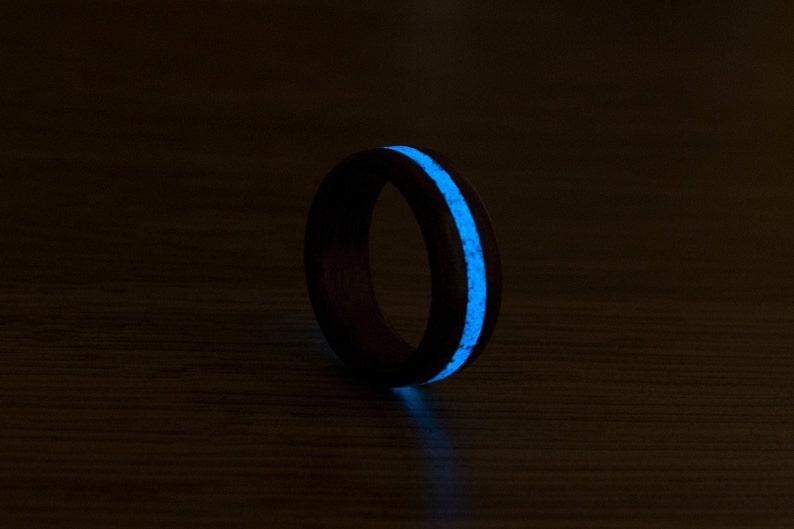 Puede incluir: Un anillo de madera negro con una incrustaci&oacute;n azul que brilla en la oscuridad. El anillo est&aacute; sobre una superficie de madera oscura.