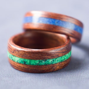 Puede incluir: Dos anillos de madera con incrustaciones de piedra verde y azul. Los anillos est&aacute;n apilados uno encima del otro.