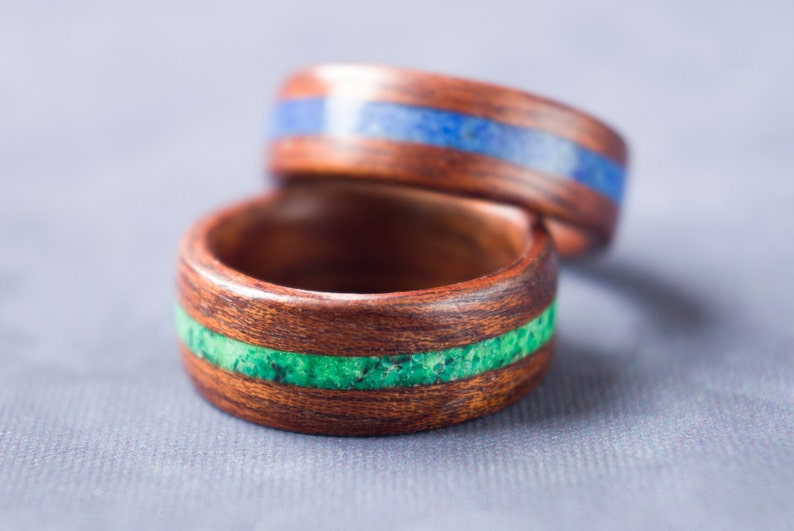 Puede incluir: Dos anillos de madera con incrustaciones de piedra verde y azul. Los anillos est&aacute;n apilados uno encima del otro.