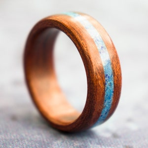 Puede incluir: Un anillo de madera con una incrustaci&oacute;n azul y blanca. El anillo est&aacute; hecho de madera oscura y tiene un acabado liso.