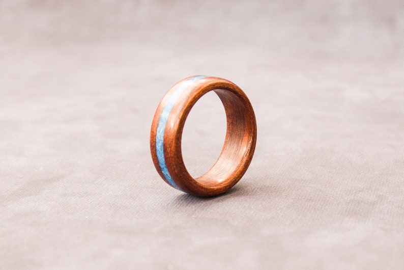 Puede incluir: Un anillo de madera con una incrustaci&oacute;n azul. El anillo es marr&oacute;n y tiene un acabado liso.
