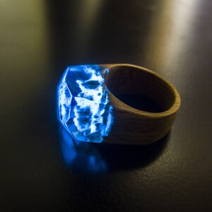 May include: A wooden ring with a blue resin inlay that glows in the dark. The resin has a unique, cloudy pattern.