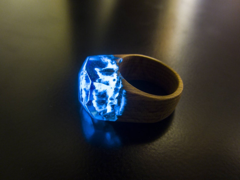 May include: A wooden ring with a blue resin inlay that glows in the dark. The resin has a unique, cloudy pattern.
