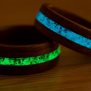 Puede incluir: Dos anillos de madera con una incrustaci&oacute;n de resina verde y azul que brilla. Los anillos est&aacute;n hechos de madera oscura y tienen un acabado liso.