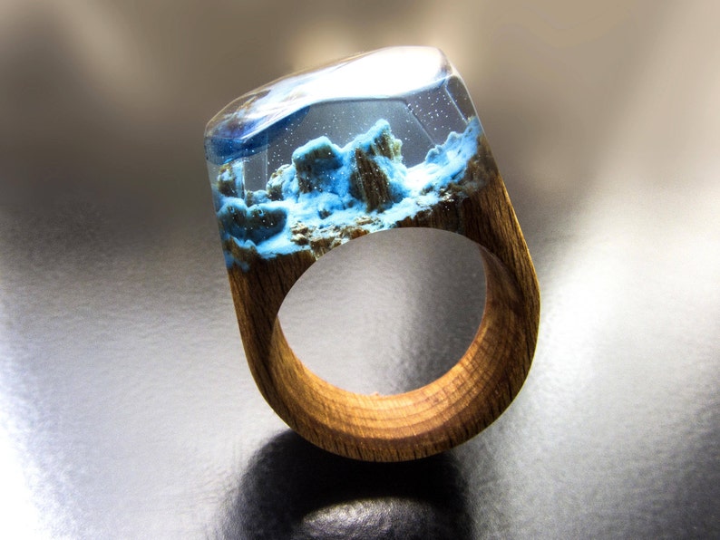May include: A wooden ring with a clear resin inlay featuring blue and white swirls and a textured, rocky design.
